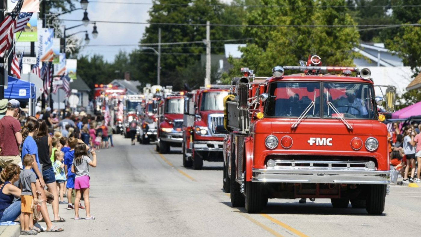 Fire trucks leading the Heritage Festival parade down Main Street as families watch from the curb